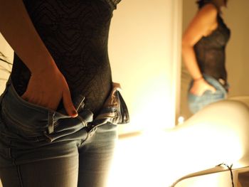 Midsection of woman removing jeans in illuminated room