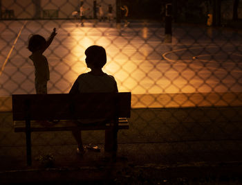 Rear view of silhouette woman with daughter on bench at night