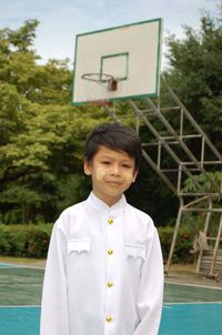 Portrait of cute boy wearing traditional clothing while standing on court against basketball hoop