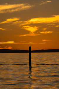 Silhouette wooden posts in sea against sky during sunset