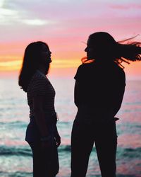 Friends standing against sea during sunset
