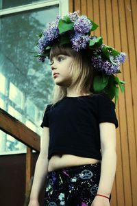 Girl looking away while wearing flowers against wooden wall