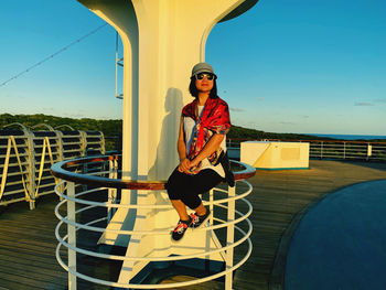 Smiling woman wearing hat sitting on railing