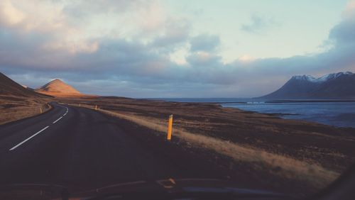 Road by lake against cloudy sky seen through car windshield