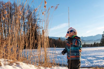 Cute boy wearing warm clothing standing on snow outdoors during winter