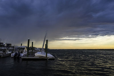 Sailboats moored in sea against sky during sunset