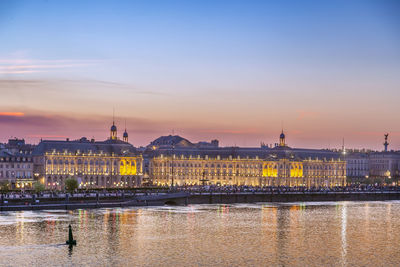 River by buildings against sky during sunset