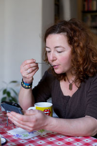 Portrait of young woman holding spoon while sitting on table