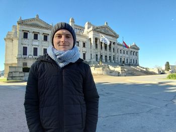 Portrait of young man standing against building in city