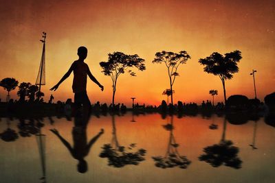 Silhouette man standing by swimming pool against sky during sunset