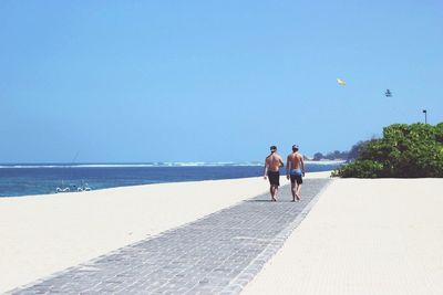 Rear view of men walking on footpath against clear sky