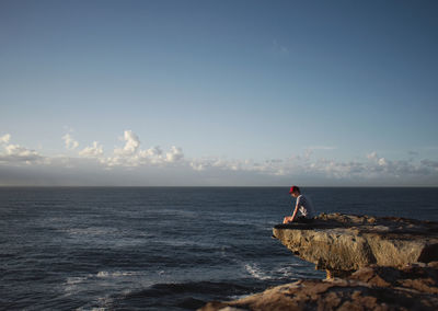 Person sitting on shore against sky