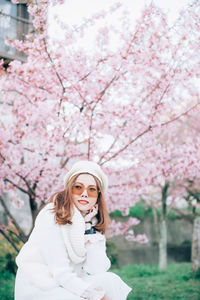 Portrait of woman standing by pink cherry blossom