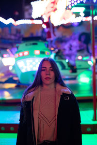 Portrait of beautiful woman standing against illuminated light at night