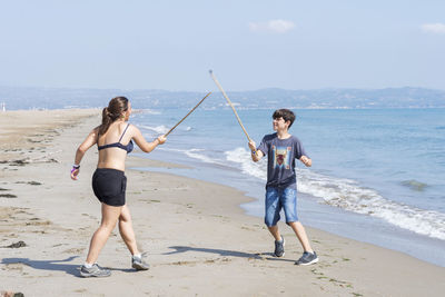 Two young friends playing with wooden swords on seashore