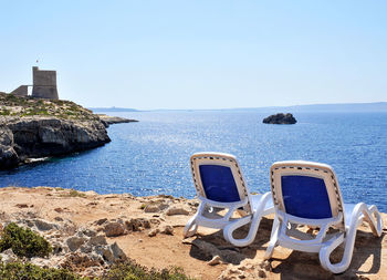 Deck chairs on rocks by sea against clear sky