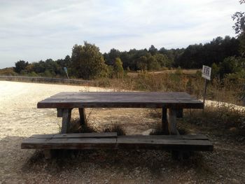 Wooden bench on field in park against sky