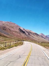 Road leading towards mountains against clear blue sky