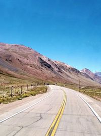 Road leading towards mountains against clear blue sky