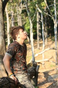 Portrait of young man standing on tree trunk in forest