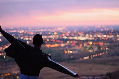 Rear view of man with cityscape in background against sky during sunset