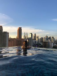 Rear view of woman in infinity pool with petronas towers in background
