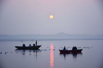 People on boats sailing in river against sky during sunrise