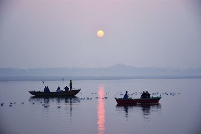 People on sea against sky during sunset