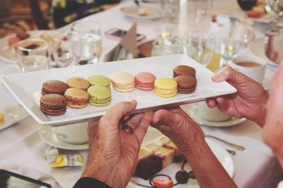 Cropped hands of friends holding macaroons in plate
