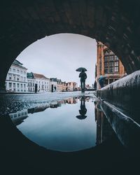 Reflection of arch bridge over river in city