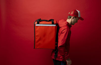Side view of delivery person carrying box against red background