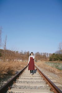 Full length of woman standing on railroad tracks against clear sky