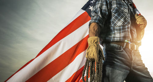 Midsection of woman holding flag against sky