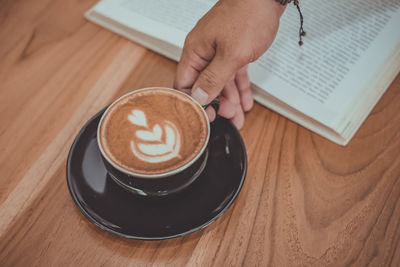Cropped hand of woman holding coffee on table