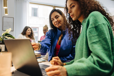 Businesswoman explaining female colleague over laptop at office