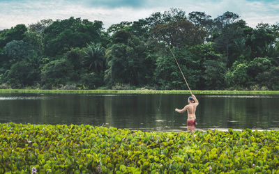 Rear view of shirtless man fishing in lake