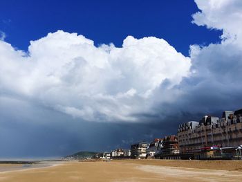 Residential buildings by beach against cloudy sky