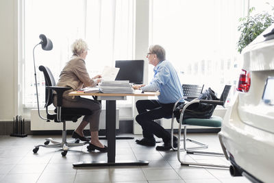 Saleswoman explaining documents at desk to man in car dealership