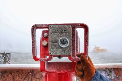 Cropped image of person holding coin-operated binoculars at harbor during winter