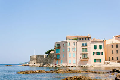 Buildings by sea against clear blue sky