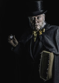 Portrait of beardy man wearing hat against black background, looking like scrooge