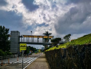 Bridge over footpath in city against sky