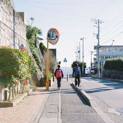 Rear view of people walking on sidewalk against clear sky