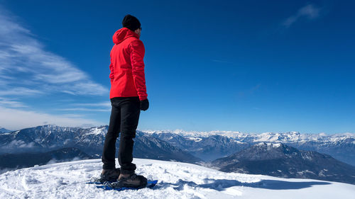 Rear view of man standing on snowcapped mountain against sky