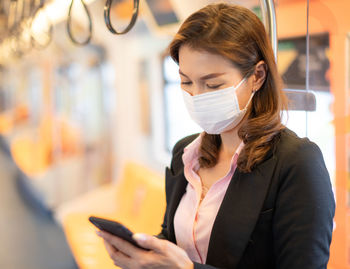 Woman wearing mask using smart phone standing in train