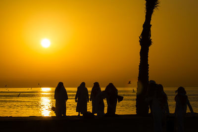 Silhouette people by sea against sky during sunset