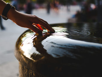 Cropped hand touching water at fountain on street