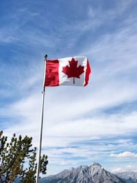 Low angle view of canadian flag waving with mountain in background against sky