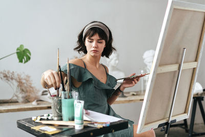 Young woman painting on canvas while sitting on table