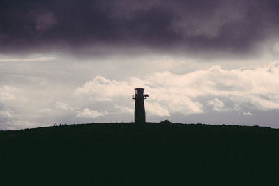 Silhouette lighthouse by building against sky